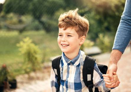 A boy holds a parent's hand as he walks to school