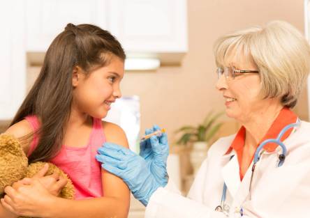 A girl holds her teddy bear as she gets a shot in the shoulder